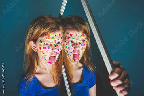 Woman with mirror sticking out tongue against blue background