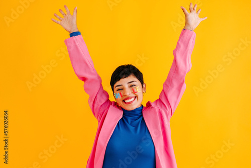 Happy young woman with arms raised standing over colored background