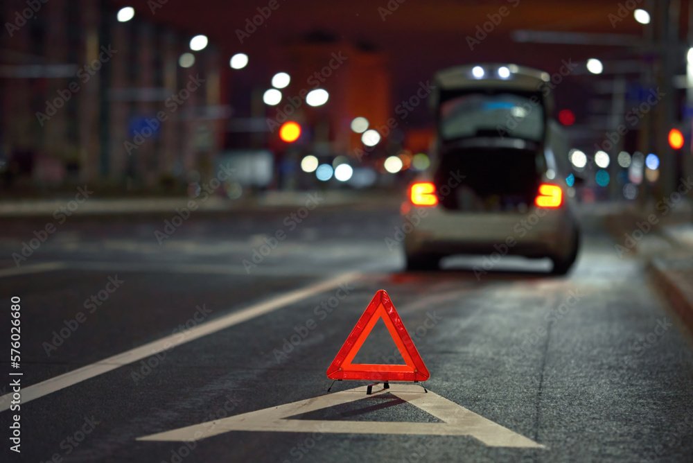 Broken down car on city street at night, red triangle - emergency stop sign behind broken blurred car. Alone damaged car at night on city highway.