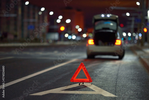 Obraz na płótnie Broken down car on city street at night, red triangle - emergency stop sign behind broken blurred car. Alone damaged car at night on city highway. w salonie