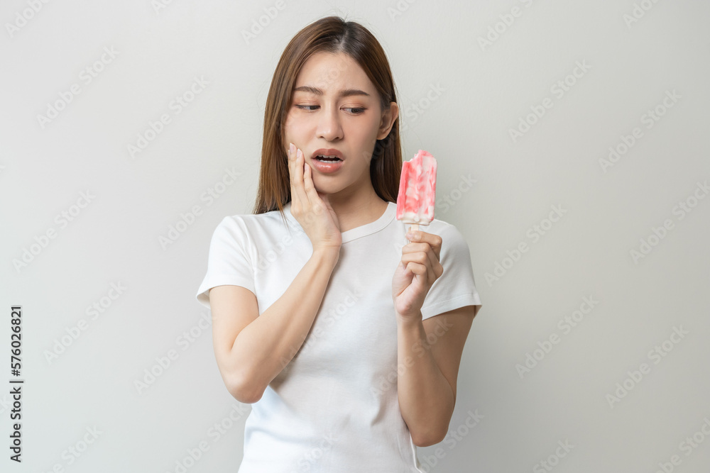 Face expression suffering from sensitive teeth and cold, asian young woman, girl hand touching her cheek, feeling hurt, pain eating ice cream, lolly. Toothache molar tooth at home, dental problem. Face expression suffering from sensitive teeth and cold, asian young woman, girl hand touching her cheek, feeling hurt, pain eating ice cream, lolly. Toothache molar tooth at home, dental problem.