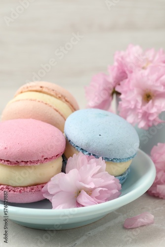 Delicious colorful macarons and pink flowers on light grey table, closeup