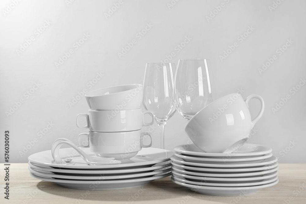 Set of clean dishware and glasses on white wooden table against light background Set of clean dishware and glasses on white wooden table against light background