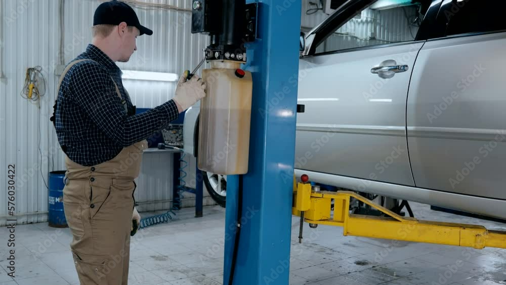 Auto mechanic lowers the car on the lift, repairing the car Auto mechanic lowers the car on the lift, repairing the car