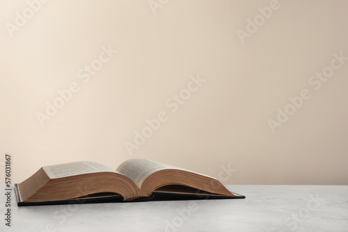 Open hardcover Bible on light grey table, space for text. Religious book