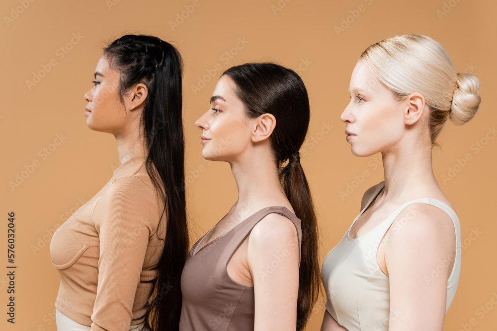 side view of blonde and brunette multiethnic women in underwear isolated on beige. side view of blonde and brunette multiethnic women in underwear isolated on beige.