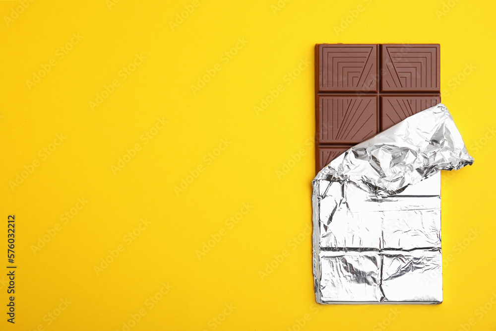 Tasty chocolate bar on yellow background, top view. Space for text