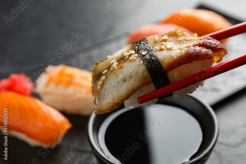 Dipping delicious nigiri sushi into soy sauce on black table, closeup