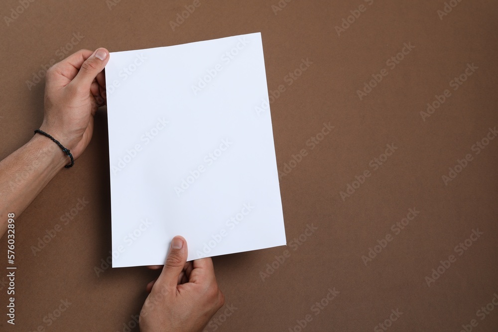 Man holding sheet of paper on brown background, closeup. Mockup for design Man holding sheet of paper on brown background, closeup. Mockup for design