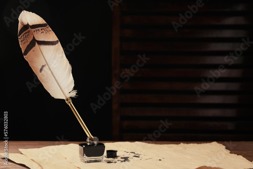Inkwell with feather pen and vintage parchment with ink stains on wooden table indoors. Space for text