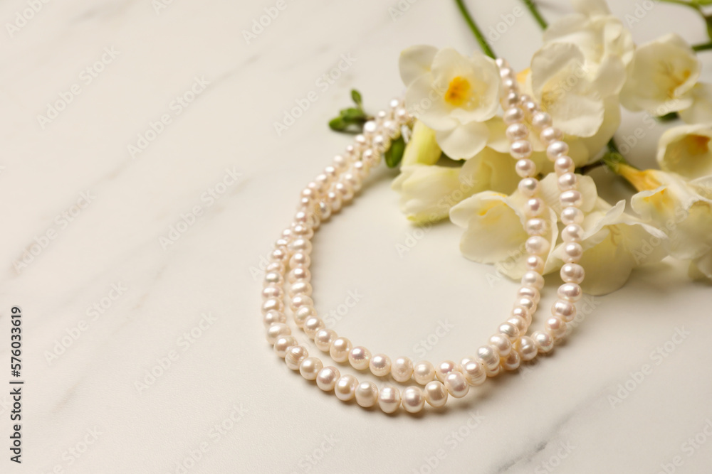 Beautiful pearl necklace and flowers on white marble table, closeup. Space for text Beautiful pearl necklace and flowers on white marble table, closeup. Space for text