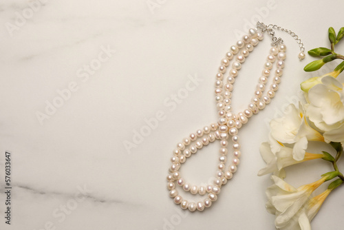 Tableau sur toile Beautiful pearl necklace and flowers on white marble table, flat lay