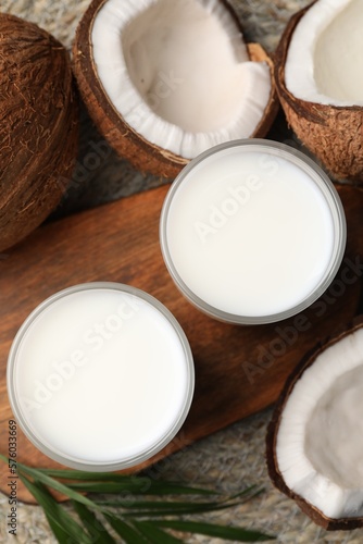 Glasses of delicious coconut milk, palm leaf and coconuts on table, flat lay