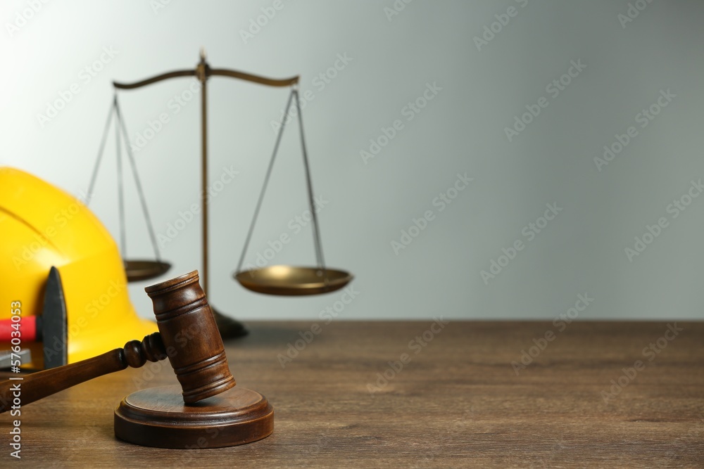 Construction and land law concepts. Gavel, scales of justice, hard hat and hammer on wooden table, space for text Construction and land law concepts. Gavel, scales of justice, hard hat and hammer on wooden table, space for text