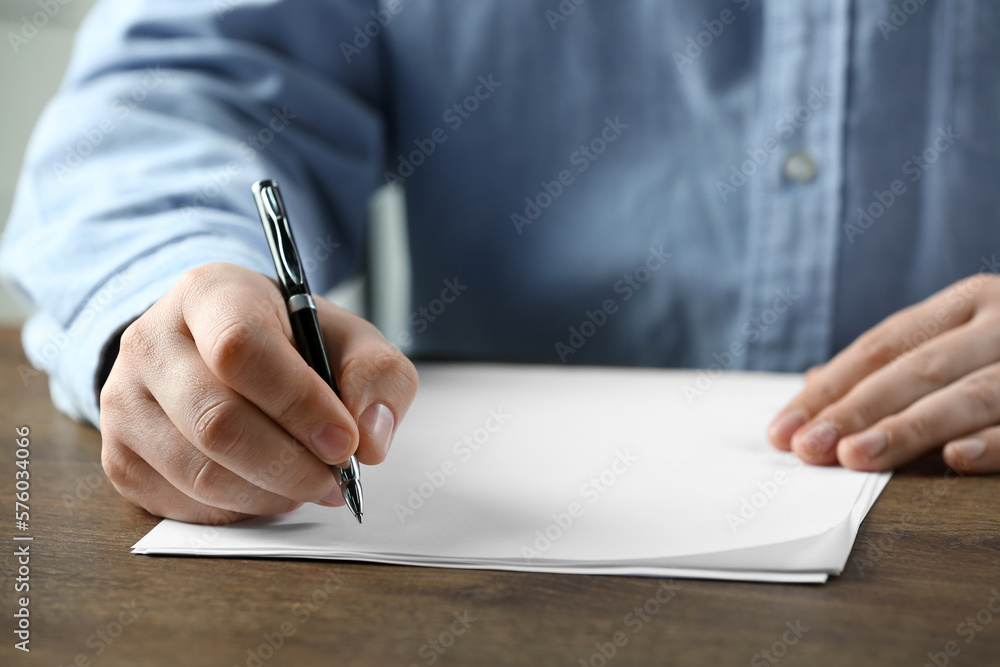 Man writing on sheet of paper with pen at wooden table, closeup Man writing on sheet of paper with pen at wooden table, closeup