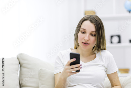 Photo of pregnant woman in white t-shirt with a phone in hand.