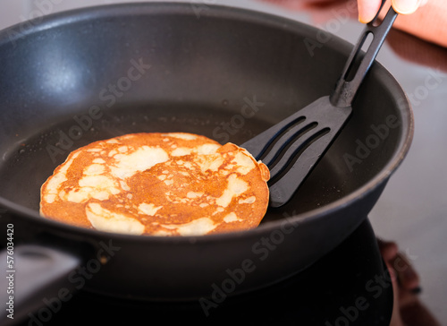 Canvas Print A pancake being flipped by a black spatula in a frying pan.