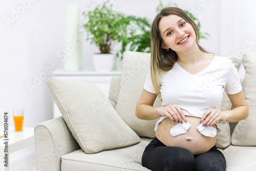 Beautiful pregnant woman with naked stomach sitting on sofa.