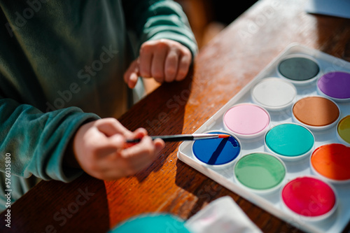 A child dips their paintbrush into a fresh pallete of watercolor paints