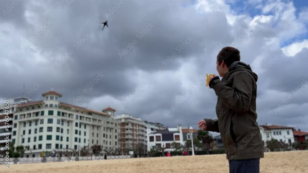 Children playing with a kite floating high in the sky on a beach during windy weather. Beautiful bay, ocean waves, turquoise water. Children playing with a kite floating high in the sky on a beach during windy weather. Beautiful bay, ocean waves, turquoise water.