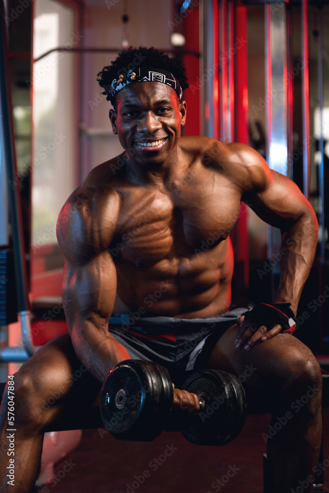 Fototapeta premium 20s Black and muscular man in a gym doing concentration curls with dumbbell