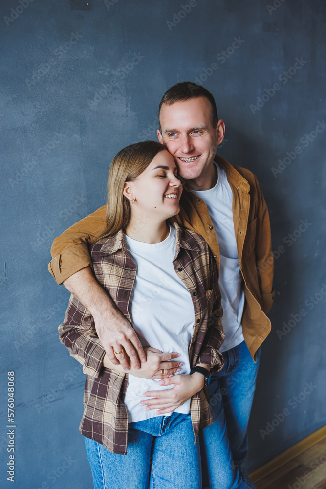 Smiling happy couple dressed in jeans and shirts standing on a gray wall background, isolated gray concrete wall background. The concept of a happy couple in love.
