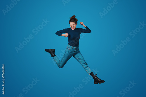Full length view of joyful woman jumping expressing positive emotions isolated over blue background. Positive person. People lifestyle portrait. Attractive