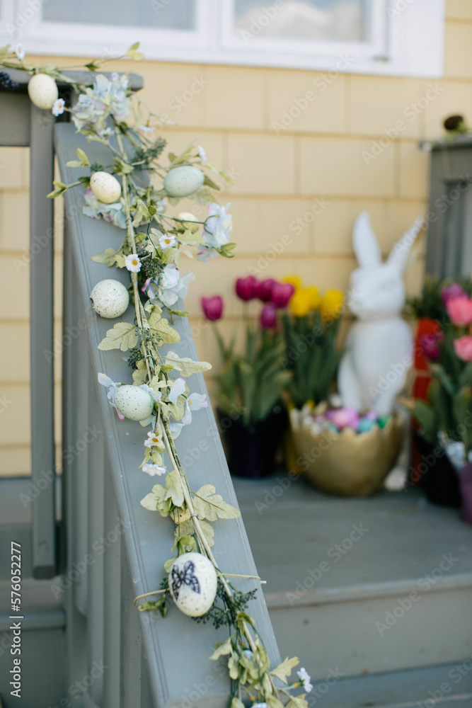 Φωτογραφία closeup of easter decor and flowers on porch in front of painted yellow house