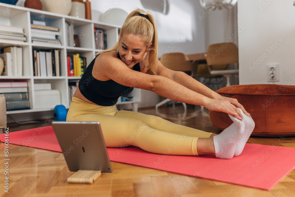Blond Caucasian woman is stretching at home on yoga mat