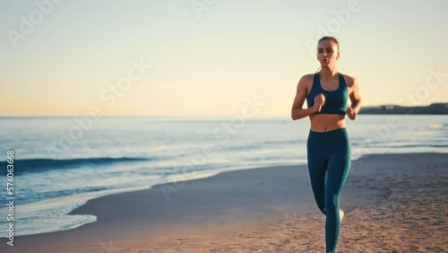 Young pretty fit woman in sportswear running on the beach. Outdoor workout by the sea. Sports and recreation, fitness and healthy lifestyle.