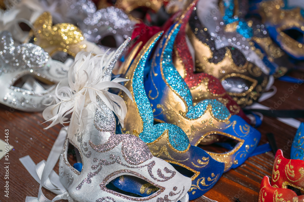 Authentic beautiful Venetian masks on a dark wooden table in Venice. Real masks of different colors and patterns for Venetian carnival on the store counter. Italian carnival traditions and decorations