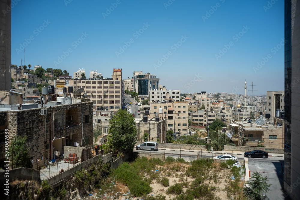 Fototapeta premium Ramallah Cityscape Between Two Walls with High White Rock Buildings, Trees and Grass