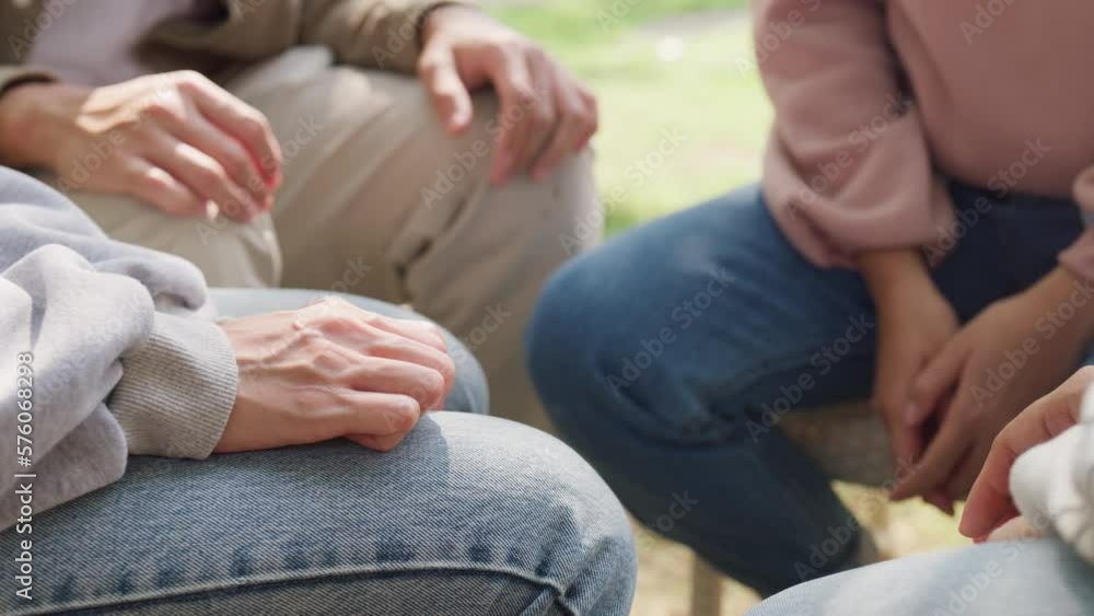 Close-up of diverse multiracial men and women group sit in circle hold hands together hope for help people in park. Support and understand at psychological therapy session, PTSD Mental health concept. Close-up of diverse multiracial men and women group sit in circle hold hands together hope for help people in park. Support and understand at psychological therapy session, PTSD Mental health concept.
