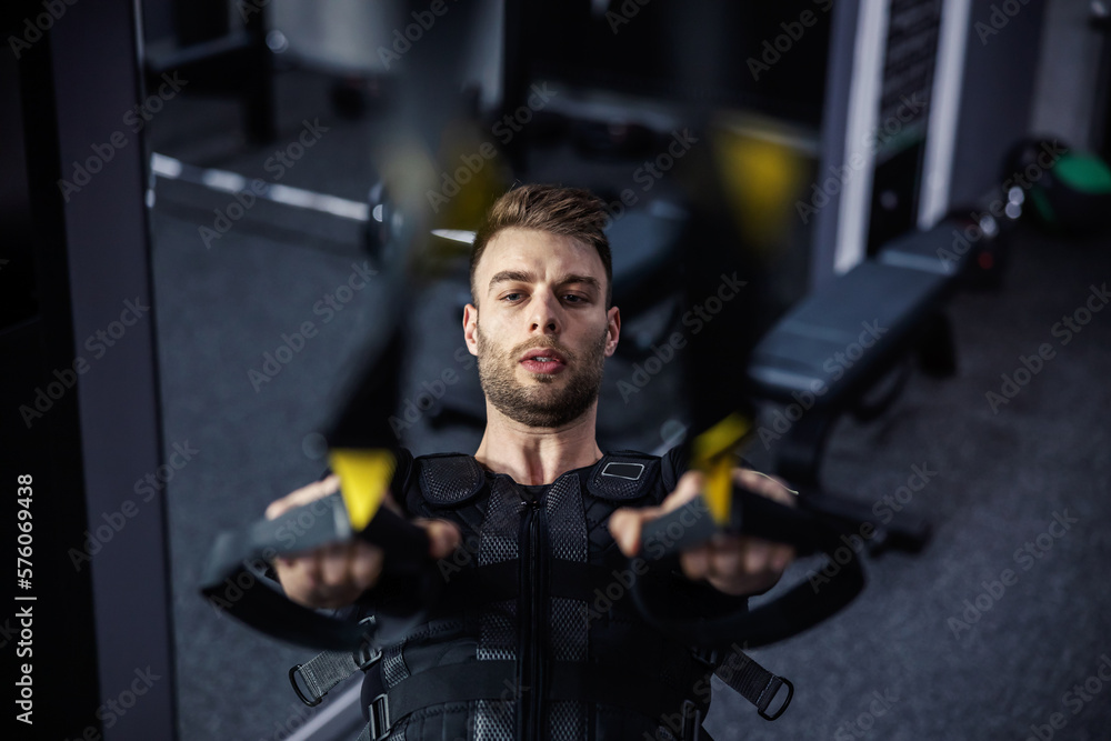 Electrical muscle stimulation training, a man keeping up a good physical shape. Exercises on a hanging bar indoors with a gray interior. Sports routine and healthy lifestyle. Concept of healthy living Electrical muscle stimulation training, a man keeping up a good physical shape. Exercises on a hanging bar indoors with a gray interior. Sports routine and healthy lifestyle. Concept of healthy living