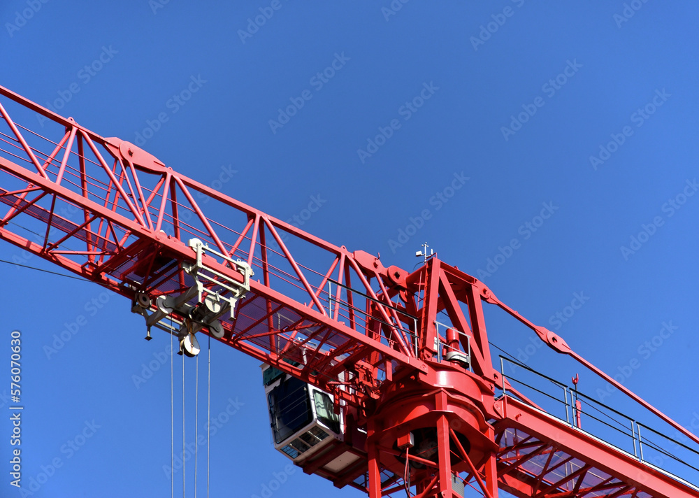 Red steel tower crane boom and vertical tower body under blue sky. truss structure and horizontal beam. white operator cabin attached on the side. building construction concept. low angle view.