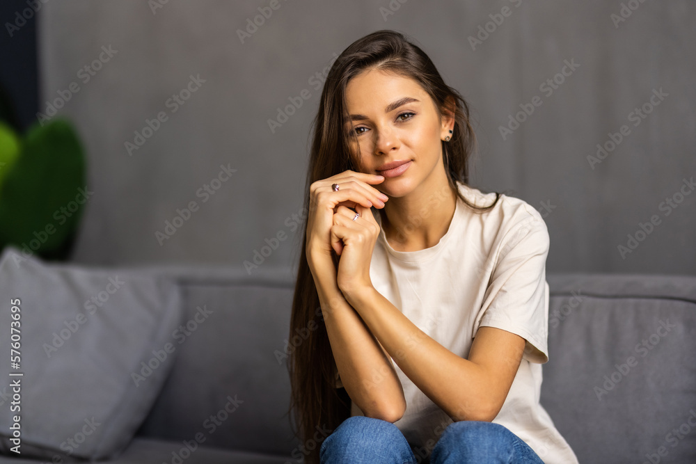 Happy young woman sitting on sofa at home and looking at camera. Happy young woman sitting on sofa at home and looking at camera.
