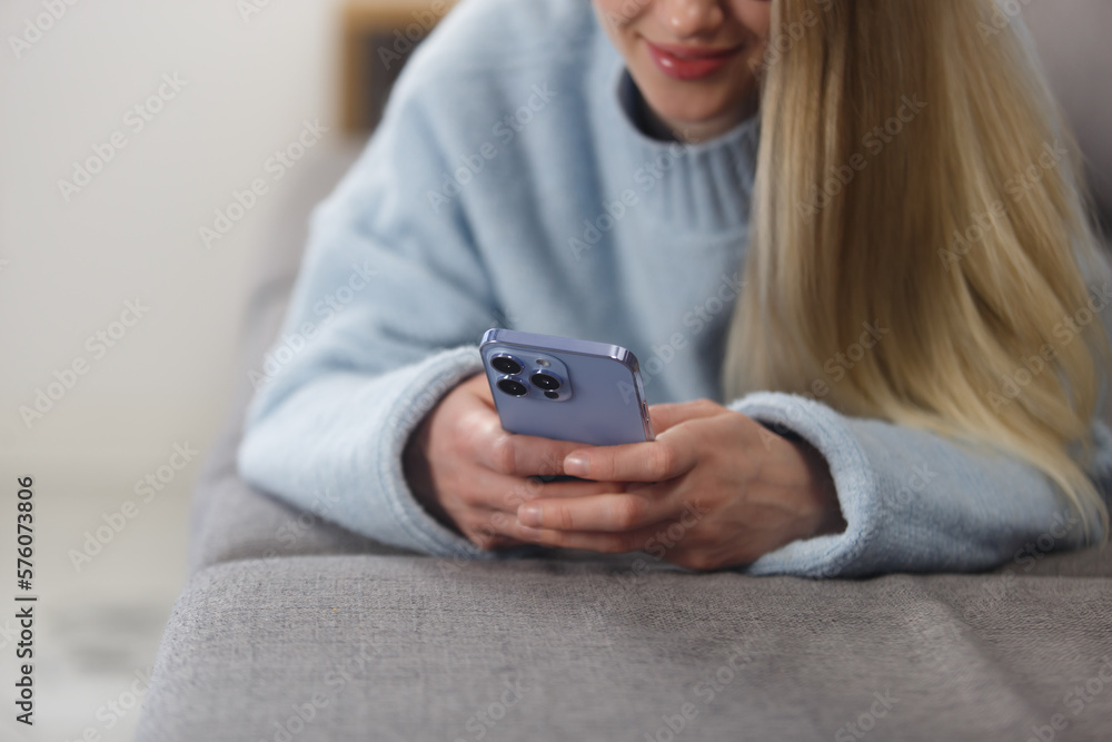 Young woman lying on couch and typing a message on a smart phone. Close up photo of white female person using modern mobile phone for communication Young woman lying on couch and typing a message on a smart phone. Close up photo of white female person using modern mobile phone for communication
