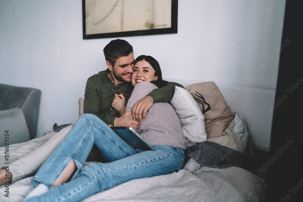 Happy couple sitting on bed together and cuddling while having laptops Happy couple sitting on bed together and cuddling while having laptops