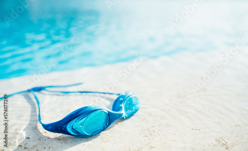 Blue Goggles on the side of swimming pool or seaside. Water and sand. Sunlit. Summer leisure activity and sports concept. Copy space