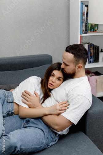 A couple in love in white t shirts and jeans is lying and hugging on the sofa.  