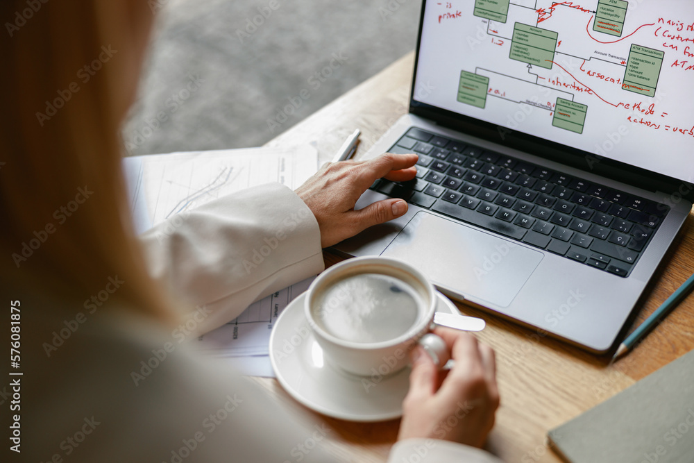 Close up of woman freelancer working on laptop and drinking coffee while sitting in cafe near window Close up of woman freelancer working on laptop and drinking coffee while sitting in cafe near window