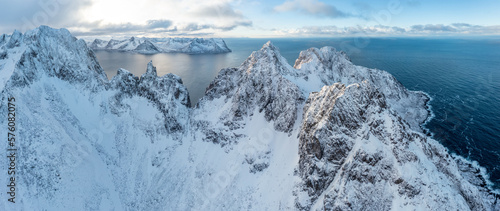 Snow covered mountain range on coastline in winter, Norway. Senja panoramic aerial view landscape nordic snow cold winter norway ocean cloudy sky snowy mountains. Troms county, Fjordgard  photo