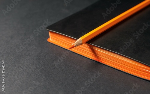 An orange pencil lies on a diary with a black cover of their eco-leather. The concept of an expensive stylish eco-friendly office. Selective focus, copy space.