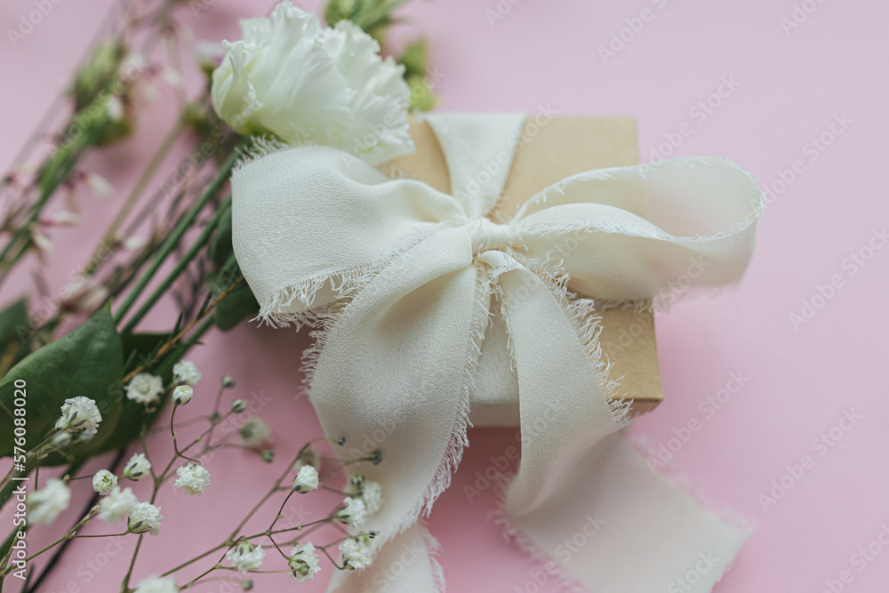 Stylish simple gift with ribbon and beautiful tender flowers on pink background. Happy womens day and mothers day concept. Season greeting card or banner Stylish simple gift with ribbon and beautiful tender flowers on pink background. Happy womens day and mothers day concept. Season greeting card or banner