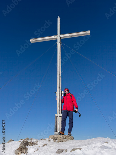 Hiker on top of peak with summit cross with snow landscape background