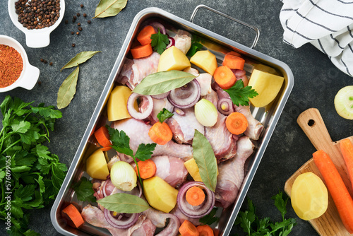 Cooking chicken bouillon or roast in cooking pan or pot with vegetables potatoes, carrots and herbs on kitchen grey concrete worktop scenery from above. Cooking preparing chicken stock. Mock up.