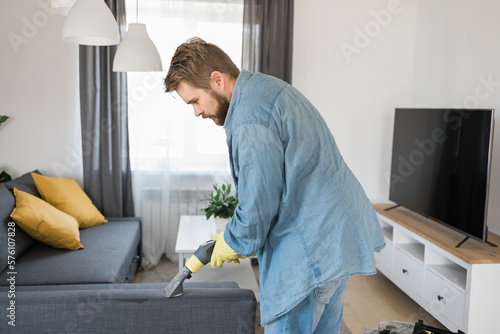 Man holding modern washing vacuum cleaner and cleaning dirty sofa with professionally detergent. Professional springclean at home concept photo
