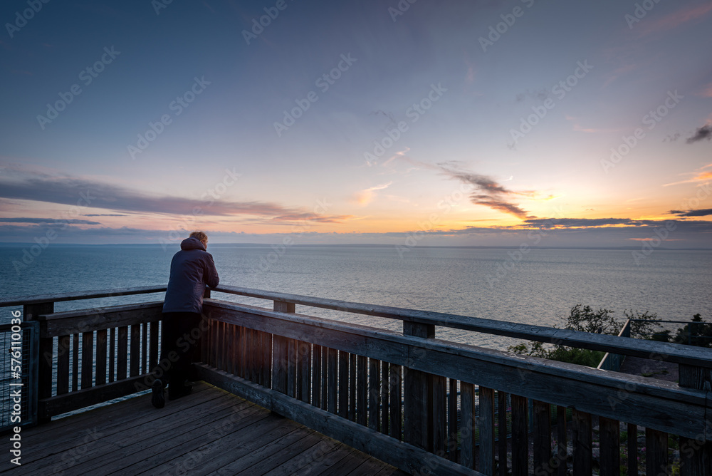 Man standing alone on view point by lake looking at sunset