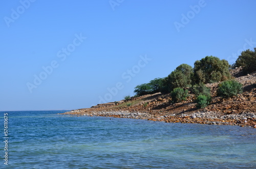 Panoramic view of the beautiful, clear blue Dead Sea shimmering and shining on a bright sunny day in Jordan and the dry land around it.