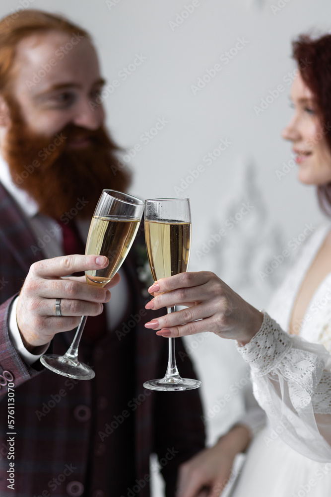 Beautiful red-hair bride in a white wedding dress and bouquet of flowers wearing pearls and a handsome groom with a red beard in a suit. Young loving couple. Drinking champagne Beautiful red-hair bride in a white wedding dress and bouquet of flowers wearing pearls and a handsome groom with a red beard in a suit. Young loving couple. Drinking champagne